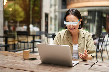 Vrouwin restaurant met koffie achter laptop, draagt lichttherapie-bril