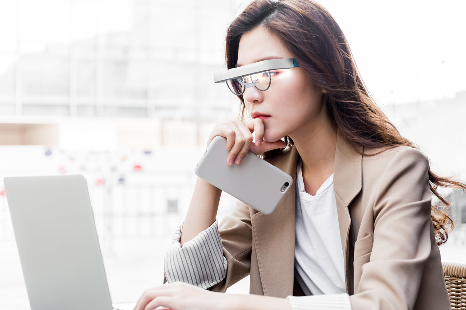 Vrouw draagt lichttherapie-bril boven haar gewone- of leesbril tijdens werk op laptop